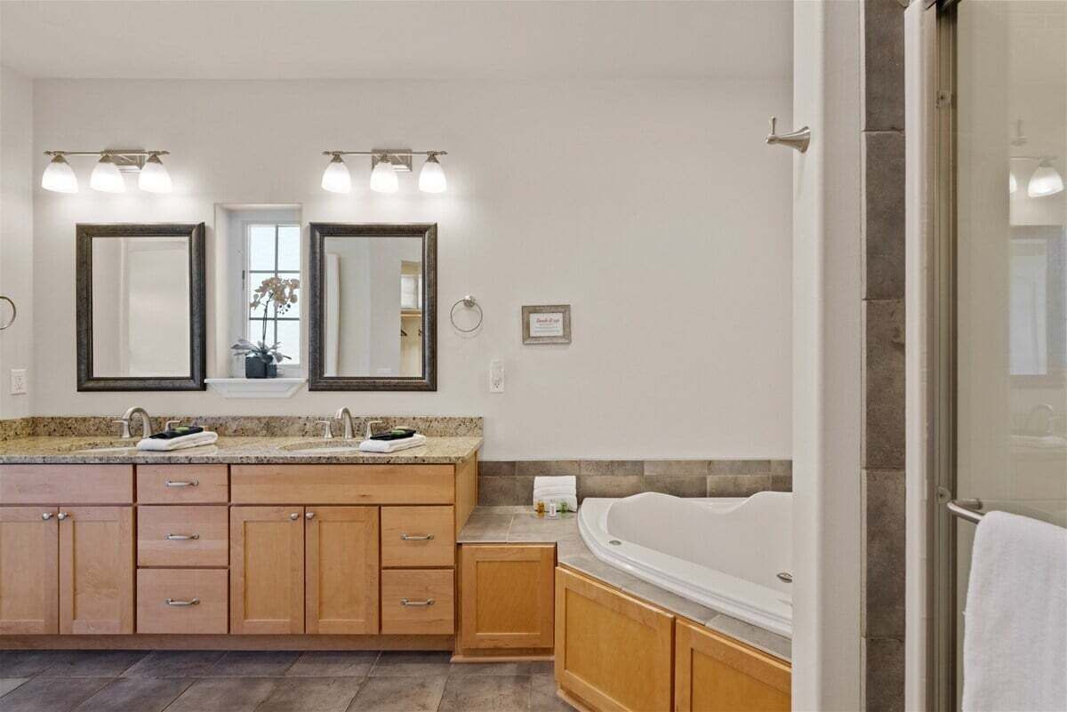 A modern bathroom with a double sink vanity, a large mirror, a bathtub, and a glass shower enclosure.