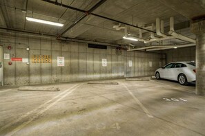 Un parking avec des murs en béton, un éclairage fluorescent et une voiture blanche garée dans un espace marqué du numéro « 301 ».