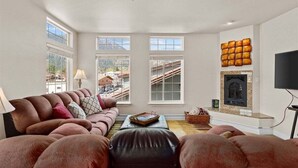 Ein Wohnzimmer mit einer Couch, einem Kamin und großen Fenstern.
