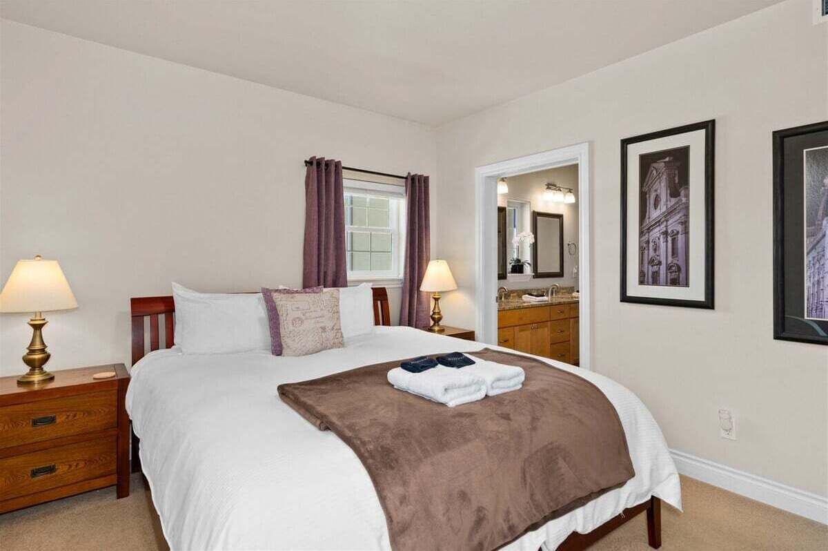 Ein Hotelzimmer mit einem Bett, zwei Nachttischlampen, einem Spiegel, einem Schminktisch und gerahmten Bildern an der Wand.