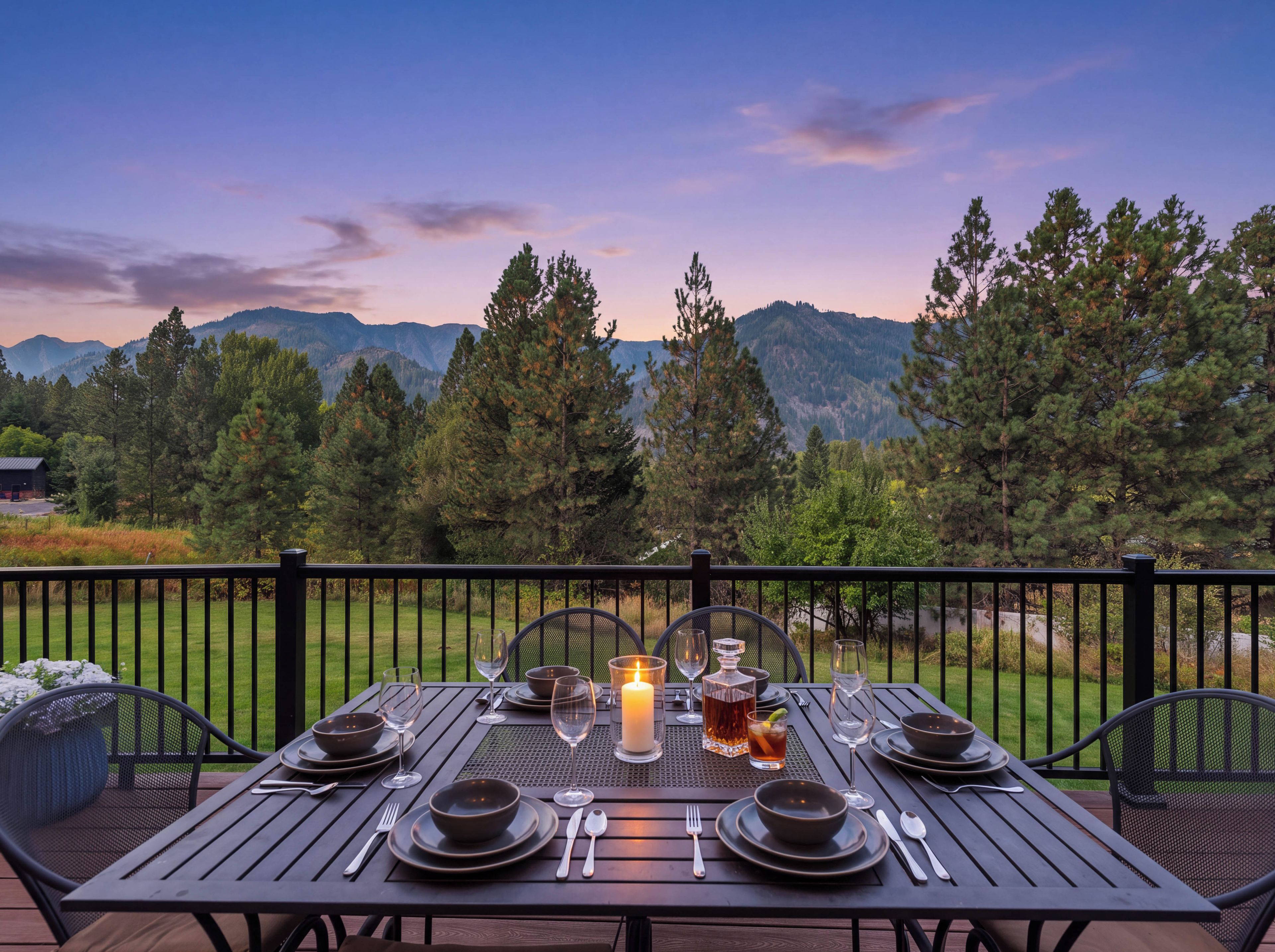 A dining table set for two with a candle, glasses, and a bottle, overlooking a mountainous landscape.