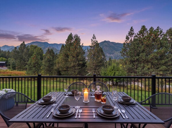 A dining table set for two with a candle, glasses, and a bottle, overlooking a mountainous landscape.