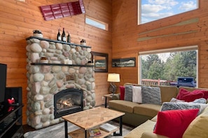A cozy room with a stone fireplace, wooden walls, a sofa, and a television.