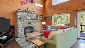 L’intérieur d’un chalet accueillant, avec une cheminée en pierre, des murs en bois, un canapé et un téléviseur.
