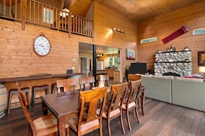 A wooden interior with a dining area, kitchen, and stone fireplace.