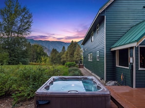 A hot tub in a backyard with a house and mountains in the background.