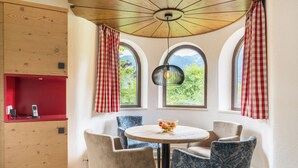 A cozy dining area with a round table, four chairs, and a view of greenery through arched windows.