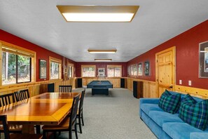 Una mesa de billar en una habitación con paredes rojas, un sofá azul y paneles de madera.