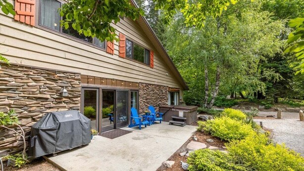 Une maison à deux étages avec une façade en pierre, un barbecue couvert, un espace salon extérieur et un jardin.