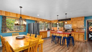 Une cuisine avec des meubles de rangement en bois, un îlot central, des tabourets de bar et une grande fenêtre avec des rideaux.