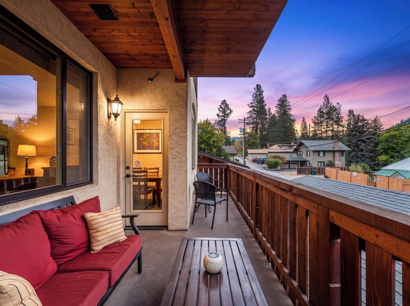 A wooden deck with a red sofa and a table, overlooking a residential street with houses and trees.
