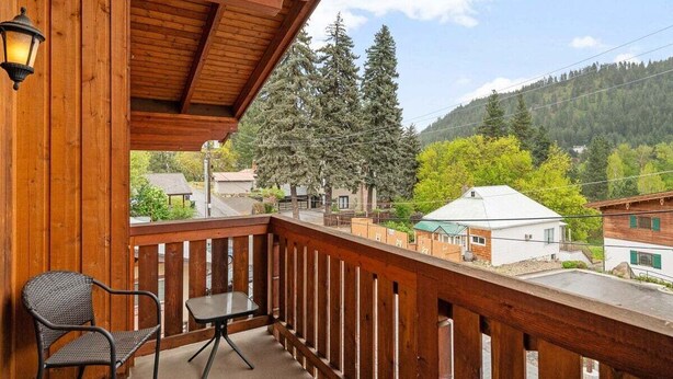 Un balcón de madera con vistas a una ladera boscosa, una silla y una mesa.
