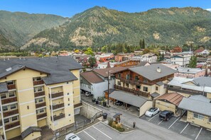 A town with a mix of residential and commercial buildings, a parking lot, and a mountainous backdrop.