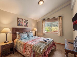 A bedroom with a large bed, two bedside lamps, a window with curtains, and a wall-mounted television. - Pet-friendly, Two-Level Condo Downtown (Leavenworth)