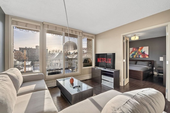A modern living room with a sofa, coffee table, TV, and large windows.