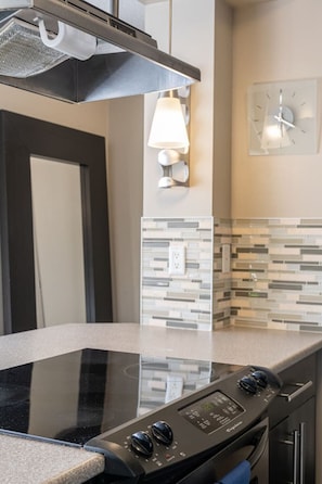 A kitchen with a black stovetop, a wall-mounted light, and a clock.