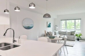 Una cucina moderna con isola centrale, illuminazione a sospensione e zona pranzo con divano e tavolino.