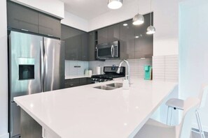 Una cocina moderna con electrodomésticos de acero inoxidable, una isla central e iluminación colgante.