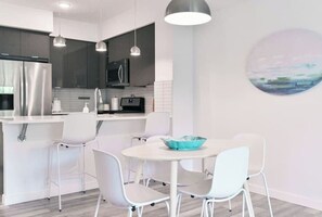 Una cucina moderna con elettrodomestici in acciaio inossidabile, sedie bianche e lampade a sospensione.