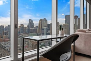 A high-rise room with a city view, a glass table, a black chair, and a beige sofa.