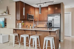 A modern kitchen with wooden cabinets, stainless steel appliances, a central island with bar stools, and pendant lighting.