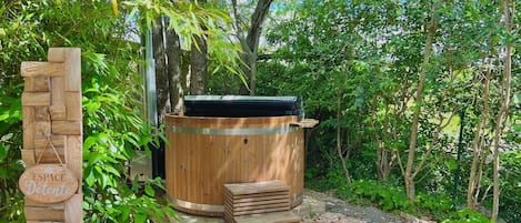 A wooden hot tub in a garden with a wooden sign that reads "ESPACE Déterte".