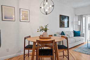 Un comedor con una mesa redonda de madera, cuatro sillas, un jarrón con plantas y una lámpara colgante moderna.
