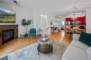 Una sala de estar moderna con chimenea, un sofá, una mesa de centro y un comedor con una cocina roja al fondo.
