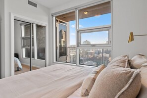 Quarto com cama grande, vista para a cidade pela janela e porta deslizante.
