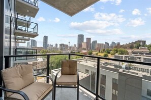 Een balkon met twee stoelen, uitzicht op een stadshemel en een moderne gevel.