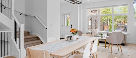 Un espace de salle à manger moderne avec une table en bois, des chaises blanches et un lustre.