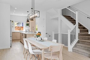 Una cocina moderna con armarios blancos, una mesa de comedor con sillas y una escalera con barandilla.