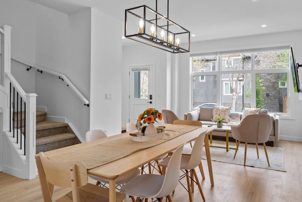 Una sala de estar moderna con comedor, una escalera y un ventanal con vistas al exterior.