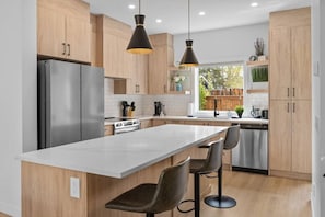 Una cocina moderna con una isla central, electrodomésticos de acero inoxidable, armarios de madera e iluminación colgante.
