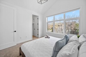 Ein Schlafzimmer mit großem Fenster, einem Bett mit weißer Bettwäsche und einem Kleiderschrank.
