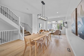 Un interior moderno con una escalera, comedor y ventanas grandes.