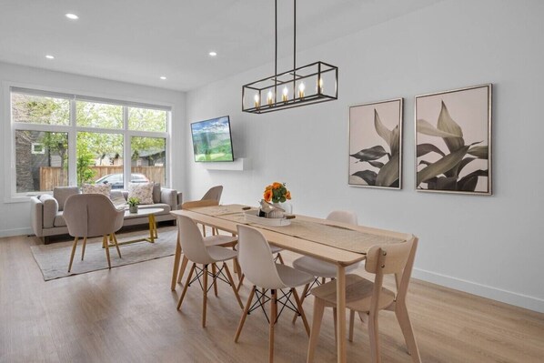 Ein moderner Essbereich mit Holztisch, weißen Stühlen und einem an der Wand befestigten Fernseher.