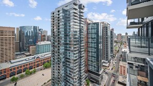 A high-rise building with a modern glass facade, surrounded by other tall buildings in an urban setting. - DT Views |UG Park | Mins to Saddledome | Gym (Calgary)