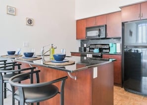 Uma cozinha moderna com armários de madeira, uma ilha central, banquetas e uma geladeira.