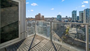 Un balcon doté d’une balustrade en verre, offrant une vue sur un paysage urbain avec de nombreux immeubles de grande hauteur.