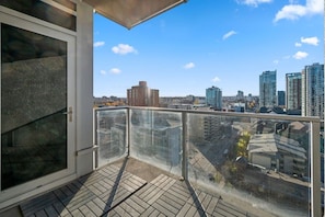 Uma varanda com guarda-corpo de vidro e vista para um horizonte urbano com edifícios altos.