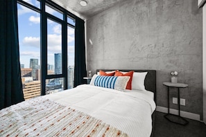 A modern hotel room with a large bed, a view of the city, and a concrete wall.