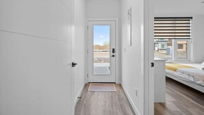 A narrow hallway leading to a bedroom with a bed, a door, and a view of the outside.
