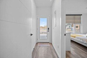 Un couloir étroit mène à une chambre qui contient un lit, une porte et offre une vue sur l’extérieur.