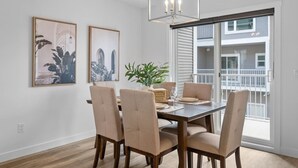 A dining area with a wooden table, beige chairs, a chandelier, and two framed pictures on the wall.