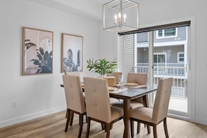 Un coin repas avec une table en bois, des chaises de couleur beige, un lustre et deux tableaux encadrés accrochés au mur.