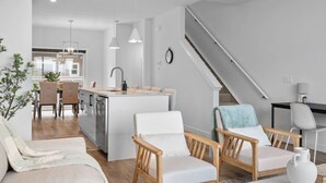 A modern living room with a sofa, two armchairs, a coffee table, and a staircase leading to an upper level.