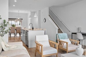 Un salon moderne comprenant un canapé, deux fauteuils, une table basse et un escalier menant à un niveau supérieur.