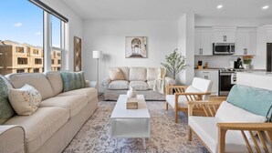 A modern living room with a sofa, armchairs, a coffee table, and a kitchen in the background.