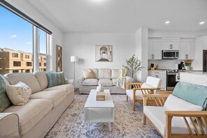 Un salon moderne avec un canapé, des fauteuils, une table basse et une cuisine en arrière-plan.